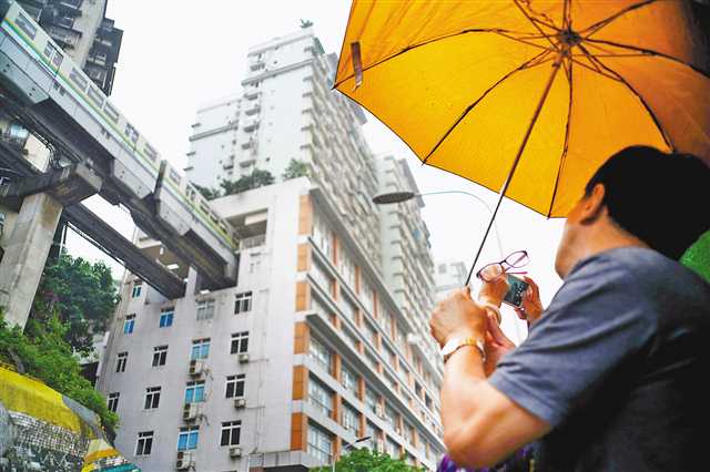5月24日,尽管重庆下着小雨,游人还是来到网红景点李子坝轻轨站拍照.